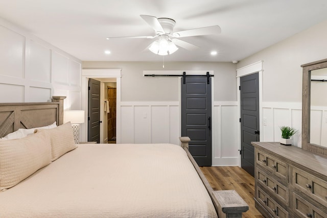 bedroom with recessed lighting, a barn door, wood finished floors, and a decorative wall
