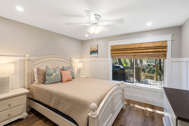 bedroom featuring a ceiling fan, a decorative wall, dark wood-style floors, and a wainscoted wall