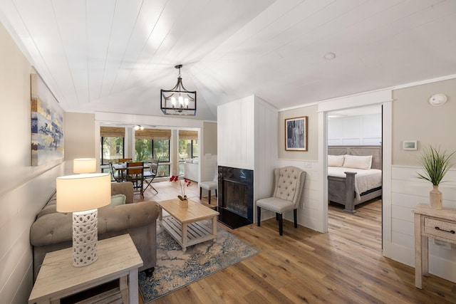 living area with a high end fireplace, a wainscoted wall, light wood-type flooring, lofted ceiling, and a notable chandelier