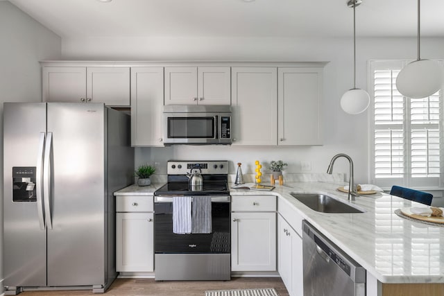 kitchen featuring light stone counters, a peninsula, stainless steel appliances, pendant lighting, and a sink