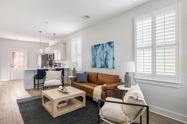 living area with visible vents, a wealth of natural light, and wood finished floors