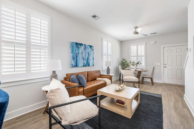 living area featuring visible vents, light wood finished floors, a ceiling fan, and baseboards