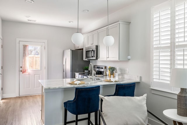 kitchen featuring appliances with stainless steel finishes, a peninsula, light wood-style floors, a kitchen bar, and a sink