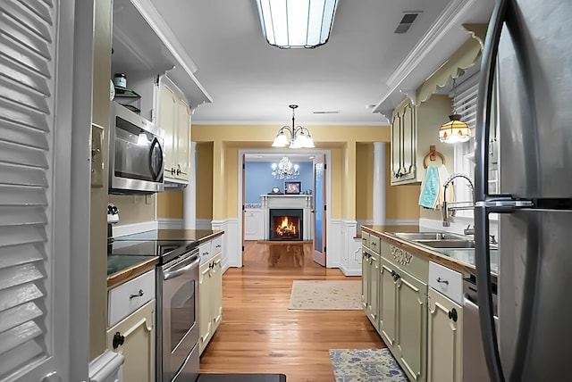 kitchen with crown molding, an inviting chandelier, a sink, light wood-style flooring, and appliances with stainless steel finishes