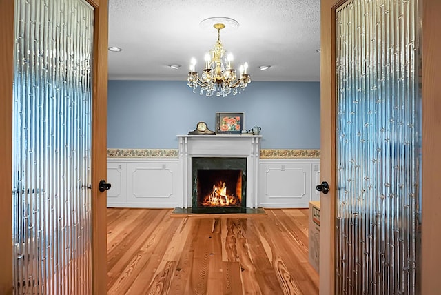 living room featuring a textured ceiling, crown molding, wood finished floors, a warm lit fireplace, and a chandelier