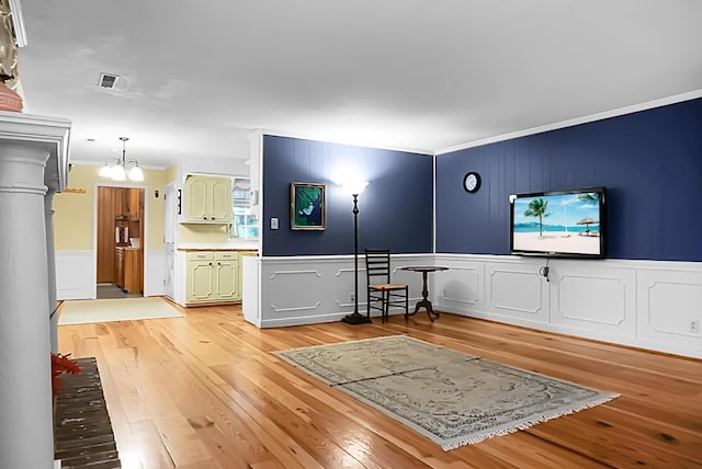 living room with light wood-style floors, ornamental molding, a decorative wall, and a notable chandelier