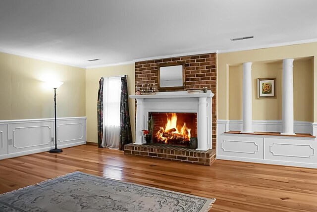 unfurnished living room with a fireplace, wood finished floors, ornate columns, visible vents, and ornamental molding