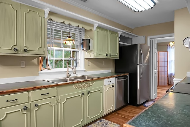 kitchen featuring dark countertops, light wood-style floors, a sink, green cabinets, and stainless steel appliances