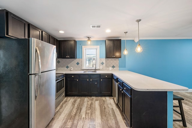 kitchen featuring decorative backsplash, light wood-style flooring, a peninsula, stainless steel appliances, and a sink