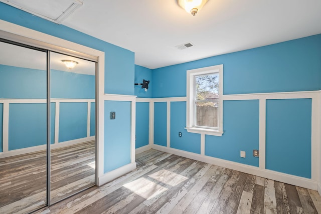 unfurnished bedroom with a closet, visible vents, a decorative wall, and wood finished floors