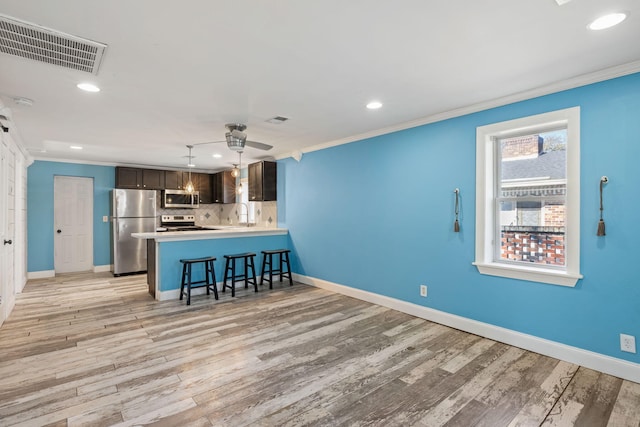 kitchen with visible vents, ornamental molding, light wood-style floors, appliances with stainless steel finishes, and a breakfast bar area