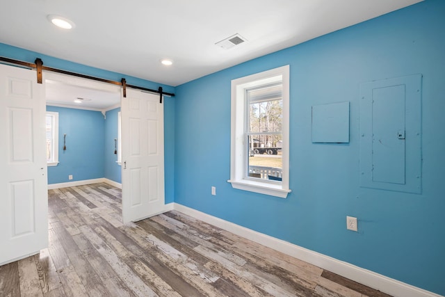 empty room featuring a barn door, wood finished floors, visible vents, and baseboards