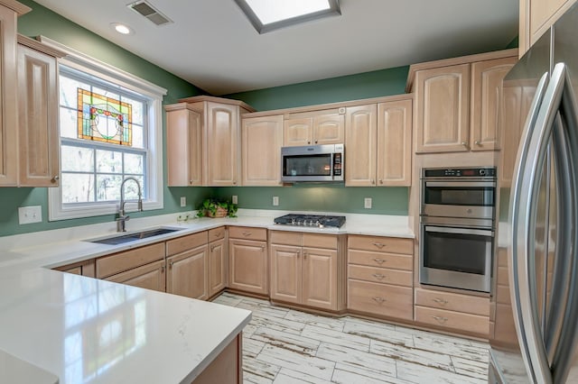 kitchen with appliances with stainless steel finishes, light brown cabinets, a sink, and visible vents