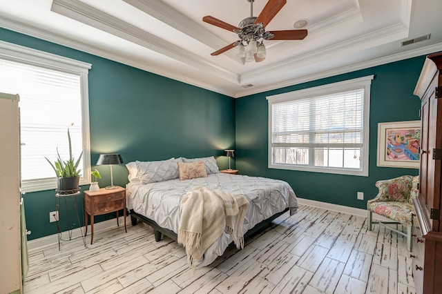 bedroom with a tray ceiling, wood finished floors, visible vents, and baseboards