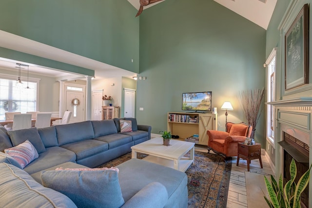 living area with high vaulted ceiling, baseboards, a fireplace, and light wood finished floors