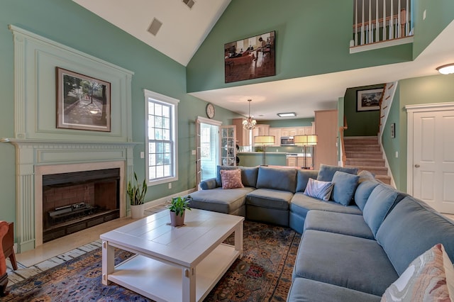 living area with a fireplace with flush hearth, high vaulted ceiling, an inviting chandelier, and stairs