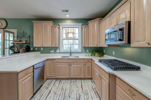 kitchen featuring stainless steel appliances, a peninsula, a sink, visible vents, and light brown cabinetry