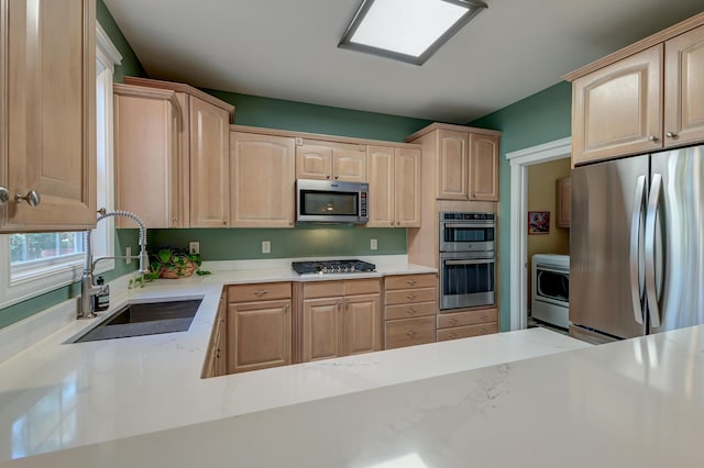 kitchen with stainless steel appliances, light brown cabinetry, a sink, and light stone counters