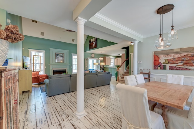 dining area featuring a fireplace, light wood-style floors, stairs, ornamental molding, and decorative columns