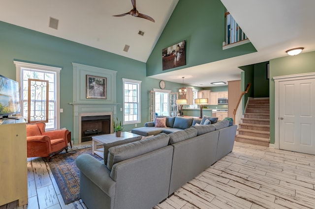 living area with a fireplace, visible vents, a ceiling fan, stairs, and light wood finished floors