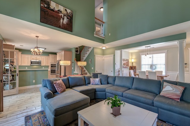 living area featuring stairs, light wood-style floors, an inviting chandelier, and ornate columns