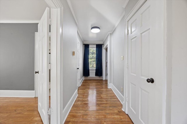 hall featuring baseboards, wood finished floors, and ornamental molding