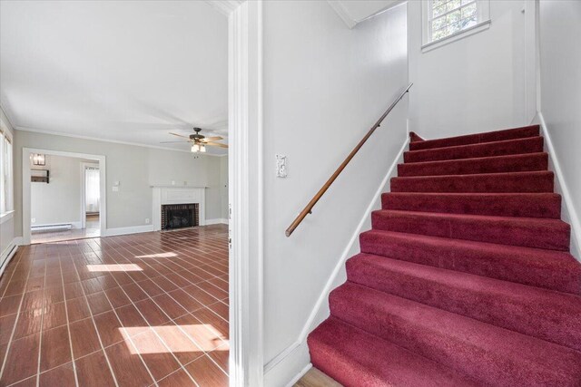 stairway with a ceiling fan, baseboards, a baseboard radiator, crown molding, and a brick fireplace