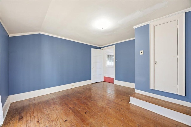 empty room featuring vaulted ceiling, hardwood / wood-style flooring, baseboards, and ornamental molding