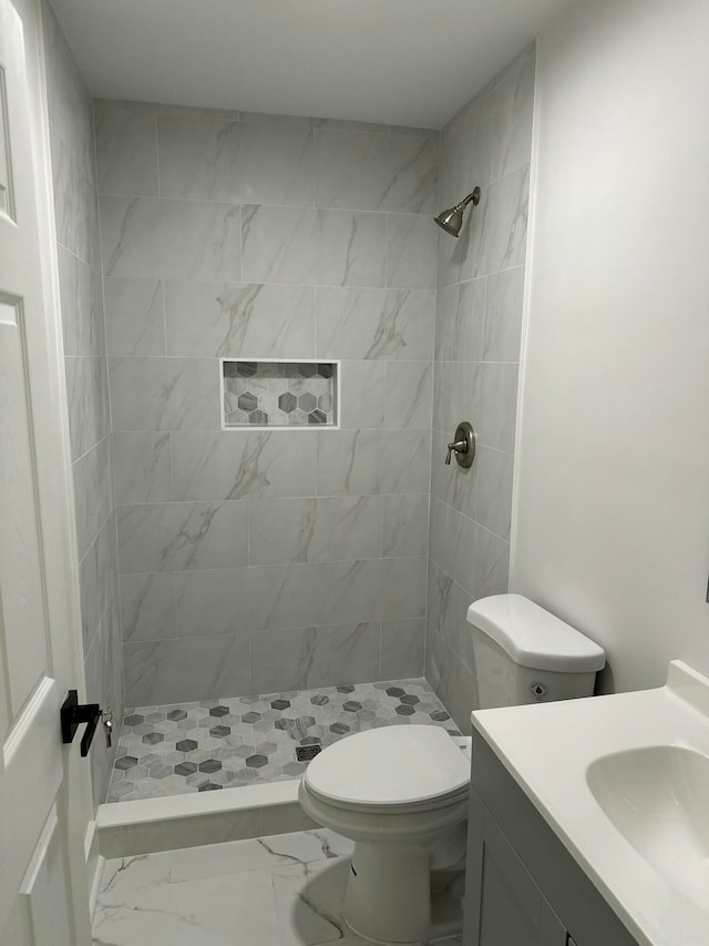 bathroom featuring a tile shower, vanity, and toilet