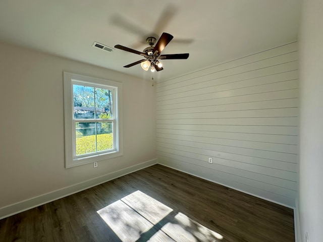 unfurnished room featuring ceiling fan, dark wood-type flooring, and wooden walls