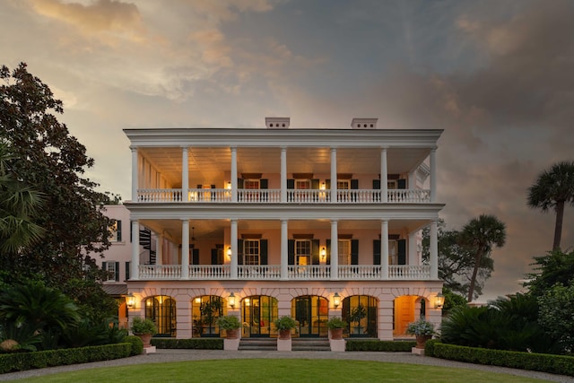 back house at dusk with a balcony and a lawn