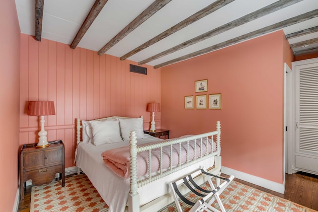 bedroom with beamed ceiling, hardwood / wood-style floors, and wooden walls