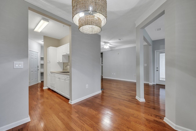 kitchen featuring sink, crown molding, light hardwood / wood-style floors, ceiling fan with notable chandelier, and white cabinets