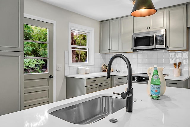 kitchen with gray cabinets, stainless steel microwave, a sink, and backsplash