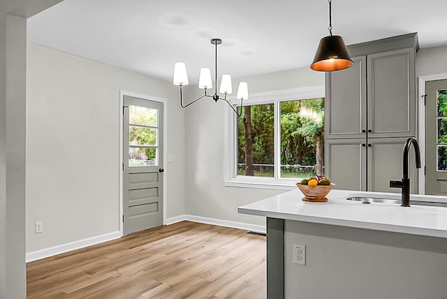 unfurnished dining area featuring a sink, light wood-style floors, baseboards, and a chandelier