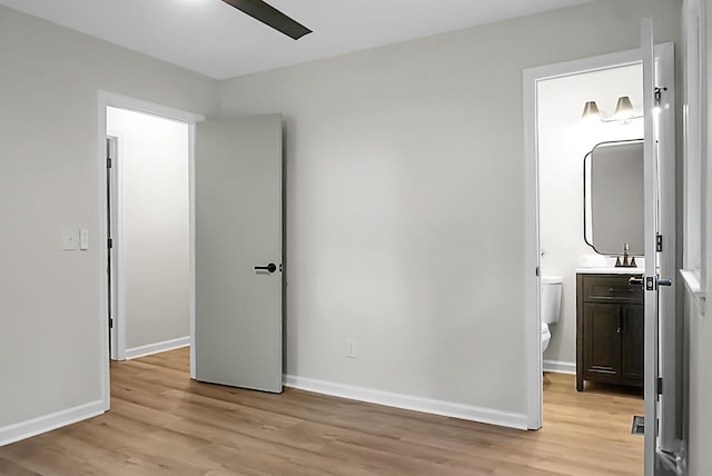 unfurnished bedroom featuring light wood-style flooring, baseboards, ensuite bath, and a sink