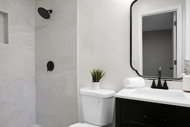 bathroom featuring tiled shower, toilet, and vanity