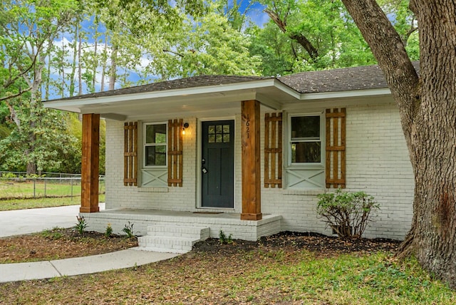 view of front facade with brick siding, a porch, fence, and roof with shingles