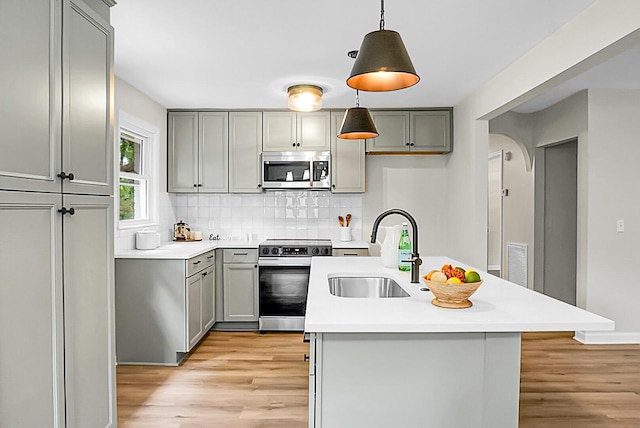 kitchen featuring stainless steel appliances, gray cabinets, a sink, light wood-style flooring, and tasteful backsplash