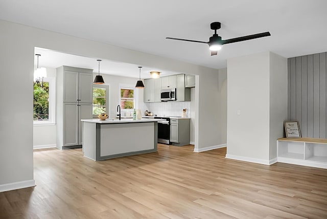 kitchen with stainless steel microwave, light wood-style flooring, gray cabinets, range, and a sink