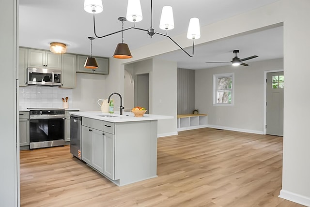kitchen featuring appliances with stainless steel finishes, a sink, light countertops, light wood finished floors, and tasteful backsplash