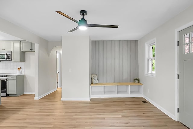 unfurnished living room with arched walkways, ceiling fan, light wood-style flooring, and baseboards