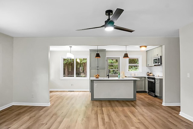 kitchen featuring appliances with stainless steel finishes, a center island, light wood-type flooring, and ceiling fan