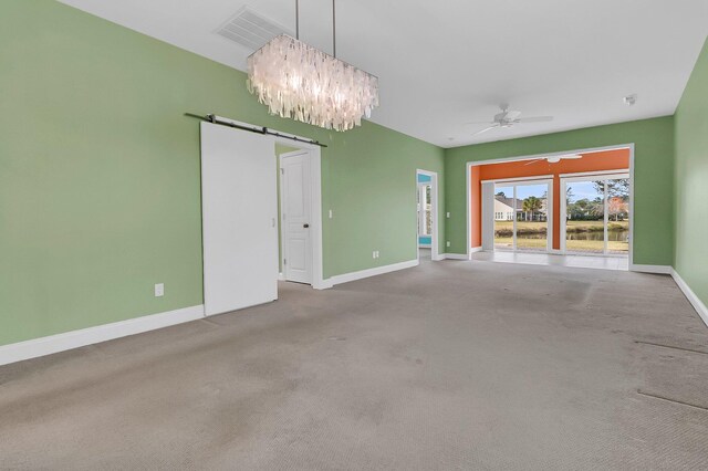 empty room with carpet flooring, ceiling fan with notable chandelier, and a barn door