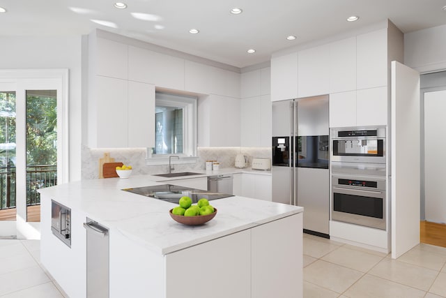 kitchen with sink, decorative backsplash, light stone countertops, appliances with stainless steel finishes, and white cabinetry