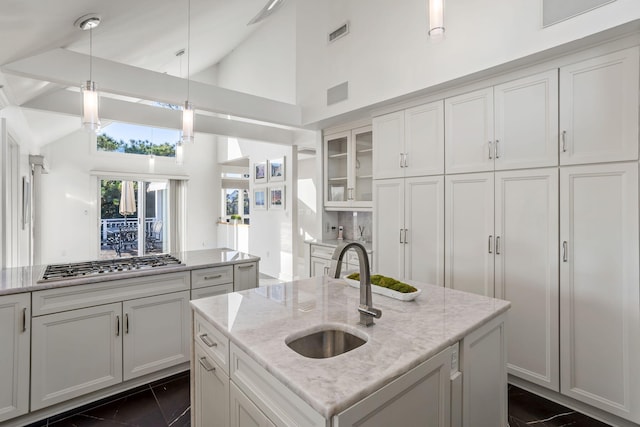 kitchen with a center island with sink, sink, light stone countertops, stainless steel gas stovetop, and high vaulted ceiling