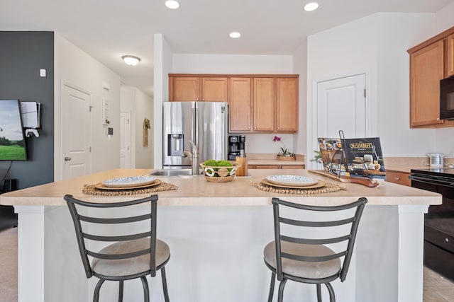 kitchen with sink, black appliances, an island with sink, and a kitchen bar