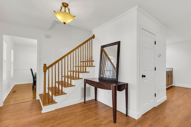 stairway with ornamental molding and hardwood / wood-style floors