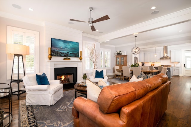 living area with recessed lighting, a fireplace, a ceiling fan, dark wood finished floors, and crown molding