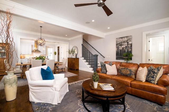 living area with crown molding, ceiling fan with notable chandelier, dark wood finished floors, and stairs